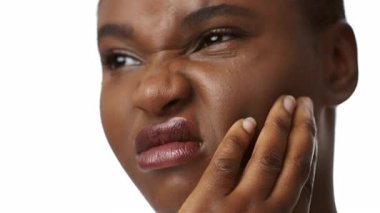 Bin yıllık Afro-Amerikan bir kadın, dişleri ağrıdığı için çenesini sağlık sigortası bağlamında tutarak rahatsızlık veriyor. Yüzündeki ifade, yalnızken hissettiği acıyı yansıtıyor..