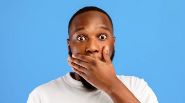 Omg. Şok olmuş Afrikalı Amerikalı adam el pozuyla ağzını kapadı. Mavi stüdyonun arka planında kameraya bakıyordu. Şaşırmış Siyah Adam 'ın Portresi. Panorama