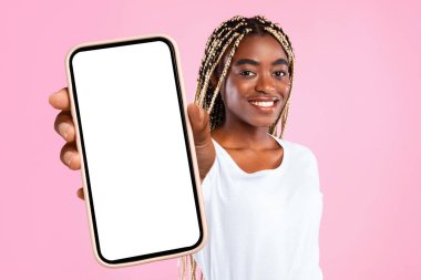 Pozitif Afrikalı genç bir bayan boş ekranlı, modern akıllı telefon gösteriyor, kullanışlı mobil uygulamalar öneriyor, pembe stüdyo arka planında izole edilmiş duruyor, kopyalama alanı