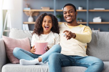 Mutlu siyah aile babası ve kızı evde film izliyorlar. Gülen Afrikalı Amerikalı baba ve liseli kız komik çizgi film izleyip patlamış mısır yiyor, kanepede oturuyor,