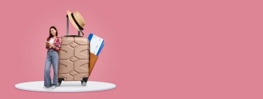 Hasır şapka ve seyahat kağıtlarıyla süslenmiş bir bavulun yanında bir turist duruyor. Yaz tatili için yer ayırtmak için telefonunu kullanıyor. Sıcak renkler tatil atmosferini çağrıştırıyor.