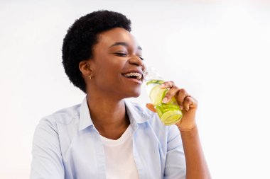 Sağlıklı su içmek ve evdeki mutfakta şişeyle serinletici pozlar vermek için şişelenmiş su içen neşeli, ince siyah kadın. Zayıflama ve kilo verme. Susuz Kalma Konsepti