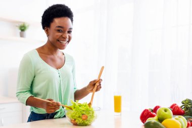 Mutfakta yemek pişiren, evde öğle yemeği için sebze salatası hazırlayan kameraya gülümseyen Afrikalı kadın. Beslenme, Zayıflama İçin Sağlıklı Yeme, Kilo Verme Tarifi