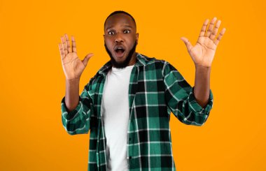 Shocked African American Guy Raising Hands Posing Looking At Camera With Opened Mouth Standing Over Yellow Studio Background. Shock Emotion Concept. Advertisement Banner.