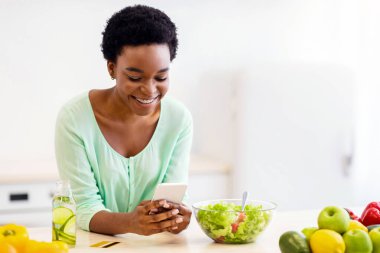 Modern Mutfak 'ta zayıflamak için akıllı telefon kullanan siyah kadın kilo vermek için sağlıklı reçeteler kullanıyor. Diyet ve Beslenme, Kilo Verme Uygulaması Konsepti
