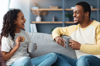 Şirin siyah baba ve kızı oturma odasında kurabiyelerle çay içiyorlar, kanepede oturup konuşuyorlar, fotokopi çekiyorlar. Mutlu Afro-Amerikan babası ve çocuğu fincanlar ve bisküvilerle atıştırıyor.