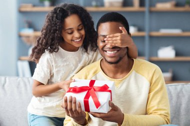 Babalar Günü konsepti, kıvırcık saçlı tatlı Afro-Amerikan kızı babasını selamlıyor, kızı mutlu babasının gözlerini kapıyor ve ona hediye kutusu veriyor, doğum gününü evde kutluyor, boşluğu kopyalıyor.