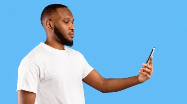 Biometric Identification. Black Man Scanning Face Using Phone Standing Posing Over Blue Studio Background. Mobile Application For Facial ID Verification And Authorization Concept. Panorama