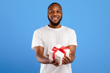 Birthday Gift. Cheerful Black Man Offering Wrapped Present Box Smiling To Camera Posing Standing On Blue Background, Studio Shot. Holiday Celebration, Presents And Gifts Concept
