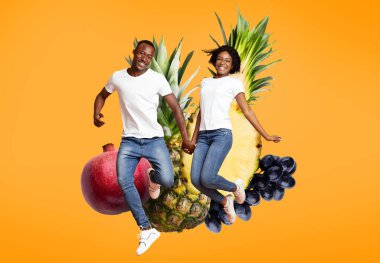 Genç bir çift, ananas ve nar gibi renkli meyve resimleriyle çevrili olarak el ele tutuşurken mutlu bir şekilde zıplıyor. Parlak arka plan onların neşeli ifadelerini arttırır..