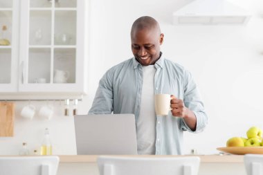 Mutfakta dizüstü bilgisayar kullanan, kahve içen, sosyal medyada gezinen, internetten haber okuyan, boş alan arayan olgun bir zenci. Sabah rutini ve modern teknoloji kavramı