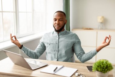 Sakin ol. Barışçıl Afrikalı İşadamı, modern ofiste stres atmak için gözleri kapalı meditasyon yapıyor. Meditasyon ve Rahatlama Egzersizi Konsepti