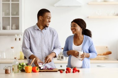 Siyahi kadın ve erkeğin evde sağlıklı yemekler pişirmesini birbirlerine bakıp gülümsemelerini, mutfağın içini görmeyi umuyorlar. Mutlu Afrikalı Amerikalı hamile çift birlikte yemek yapıyor.