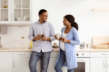 Siyah bir ailenin mutfakta kahve içmesini, konuşmasını ve birbirine bakmasını beklemeyi seviyorum. Neşeli Afro-Amerikan hamile kadın ve fincanlı kocası, kurabiyeli bitki çayının keyfini çıkarıyorlar.