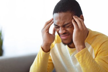 Evde baş ağrısı çeken, şakaklarına dokunan, fotokopi alanı olan, arka planda bulanıklık olan siyahi bir gencin yakın çekimi. Migren, baş ağrısı, stres, gerilim sorunu, akşamdan kalma konsepti