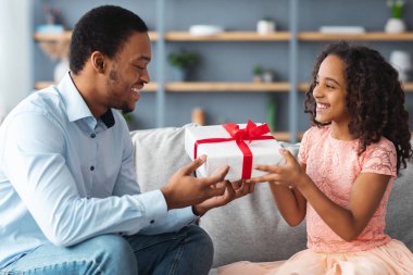 Afro-Amerikan baban ve tatlı kızın evde Babalar Günü 'nü kutluyor. Sevimli siyah kız, gülümseyen genç babasını selamlıyor, ona sarılıyor ve hediye kutusu veriyor, oturma odası içi, fotokopi odası.