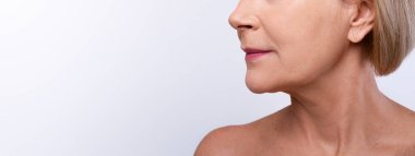 Olgun cilt tazeleme kavramı. Gri stüdyo arka planında çıplak omuzlu olgun bir kadın görüntüsü, kopyalama alanı. Mükemmel dudakları ve afiş tasarımı olan tanınmayan son sınıf öğrencisi bayan.