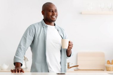 Hayalperest Afro-Amerikalı adam mutfakta kahve içiyor, pencereye bakıyor, hafta sonları sıcak içkinin tadını çıkarıyor, bedava. Hayatın ahengi