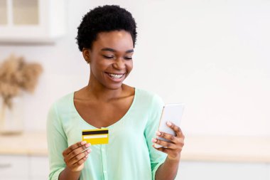 Market Teslimat Başvurusu. Siyah kadın kredi kartı kullanıyor. Modern mutfaktaki yiyecek ve sebze siparişi veriyor. İnternetten alışveriş uygulaması. Seçici Odaklanma