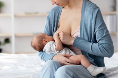 Eksiklik Konsepti. Gülümseyen güzel bir kadın bebeğini evde emziriyor, Milenyum annesi yatakta oturuyor, bebeğini emziriyor, anneliğin ve anneliğin tadını çıkarıyor,