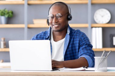 Yardım hattı destek servisi. Afrika kökenli Amerikalı çağrı merkezi operatörü merkez ofiste dizüstü bilgisayarla çalışıyor, bilgisayar ekranına bakıyor ve gülümsüyor.