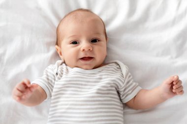 Yakından çekilmiş, yatakta uzanan ve kameraya gülümseyen sevimli bir bebeğin portresi çizgili bir kaç aylık bebek, beyaz çarşaflarda dinlenen, boş alan.