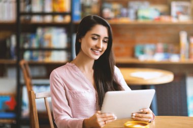 Kullanışlı bir uygulama. Dijital tablet kullanan, kafede oturan, fotokopi çeken mutlu Latin bayan. Gülümseyen ve kafeteryada çalışan olumlu bir kadın. SMM-yöneticisi, serbest çalışan, işini yapan blogcu