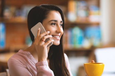 Kafede kahve içerken akıllı telefonda konuşan mutlu Latin bayan, fotokopi alanı. Kafeteryada tek başına vakit geçirirken cep telefonuyla konuşan olumlu bir kadın.