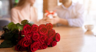 Kafedeki masada duran bir buket güzel kırmızı gül ve arka planda sevgililer günü hediyelerini veren milenyum çifti, fotokopi alanı. Panorama. Tatil kutlaması