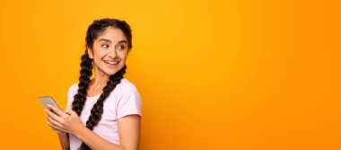 İnsanlar ve Teknoloji. Cep telefonu kullanan ve bedava fotokopi alanına bakan gülümseyen genç Hintli kadının portresi sarı stüdyo arka plan duvarında izole bir şekilde duruyor.