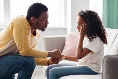 Siyah bir baba, üzgün kızını rahatlatıyor, iç mekan, yan manzara. Şefkatli Afrikalı Amerikalı baba, kavga üstüne, üzgün kızı teselli ediyor. Babalık, ebeveynlik, aile ilişkileri kavramı.