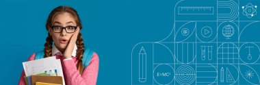 Bir öğrenci parlak bir mavi arkaplanın önünde duruyor, bir yığın çalışma malzemesi tutarken gözle görülür şekilde şaşırmış. Atmosfer öğrenme ve eğitime olan heyecan ve bağlılığı yansıtıyor.