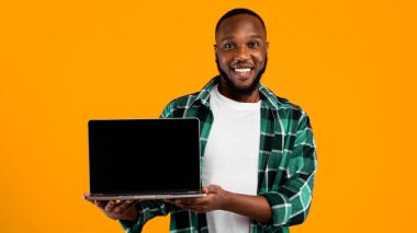 Gülümseyen Afrikalı Adam Laptop Boş Ekranı Sarı Stüdyo Arkaplanında Duran Harika Web Sitesini Öneren Kameraya Gösteriyor. Çevrimiçi Servis Reklamı. Model