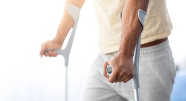 Koltuk değneği kullanan genç bir adamın bacak yaralanması ya da kırık kemik görmesi. Tanımlanamayan Afro-Amerikan hasta içeride hareket desteğiyle yürüyor, yakın plan.