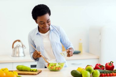 Modern mutfaktaki yağlı sebze salatasını pişiren neşeli Afrikalı kadın. Kilo kaybı ve Diyet Konsepti için Sağlıklı Beslenme ve Yemek Tarifleri