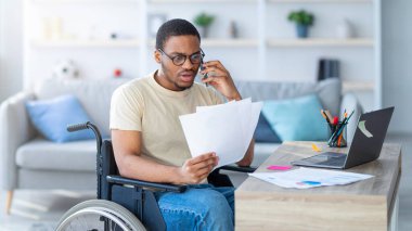 Özürlü insanlar için internet işi. Evrakları olan genç siyahi bir adam evde dizüstü bilgisayarın önünde telefonla konuşuyor. Milenyum tekerlekli sandalyedeki adamın uzaktan kumandalı işi var, mobil cihazla iletişim kuruyor.