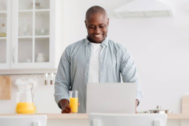 Mutlu Afro-Amerikalı olgun bir adam portakal suyu içip dizüstü bilgisayarda film izliyor, hafta sonları sabah keyfine bakıyor ve evde dinleniyor.