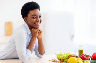 Sağlıklı beslenme. Evde sebzelerle dolu bir masanın yanında kameraya gülümseyen siyah bir kadın poz veriyor. Kilo verme uygulaması, beslenme ve sağlık. Profesyonel Diyetisyen Portresi