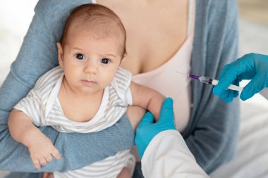 Aşı kavramı. Tanınmayan bir çocuk doktoru klinikteki küçük bebeğe aşı yapıyor, bebek bağışıklığını güçlendiriyor, kameraya bakan korkmuş bir çocuk için iğne yapıyor,