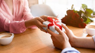 Milenyum erkeğinin sevgilisine sevgililer günü hediyesi ya da rahat bir kafede doğum günü hediyesi verirken yakın plan görüntüsü. Tanımlanamayan genç bir çift özel bir olayı kutluyor, hediyelerini değiş tokuş ediyorlar.