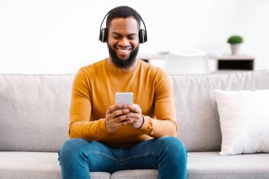 Cep telefonunda müzik dinleyen Afrikalı bir adam ya da evdeki koltukta oturan kulaklık takan internet üzerinden öğrenen bir adam. Müzik Aşığı Konsepti için Mobil Uygulama