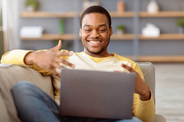 Gülümseyen siyahi adamın arkadaşlarıyla görüntülü konuşma yapması, evde dizüstü bilgisayar kullanması, defter ekranına bakması, konuşması ve el kol hareketi yapması, kopyalaması. Çevrimiçi iş görüşmesi yapan neşeli Afrikalı adam.