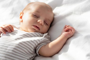 Sevimli bir bebeğin yatakta uyuması, beyaz çarşafta uyuması, gündüz vakti uyuması, evde dinlenmesi, kesilen görüntüler.