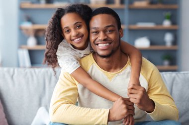 Evlerinde eğlenirken kucaklaşan mutlu siyah baba ve kızın yakın plan portresi, kopyalama alanı. Gülümseyen Afrikalı Amerikalı liseli kız neşeli babasına arkadan sarılıyor.