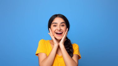 Omg. Heyecanlı, neşeli ve neşeli Hintli bayanın portresi gülümseyen, dokunan ve kameraya bakan, olumlu duygularını ifade eden, mor stüdyo arka planında tek başına duran,