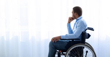 Engellilik ve depresyon. Tekerlekli sandalyedeki genç siyahi bir adamın kendini dünyadan soyutlaması, evden dışarı bakması. Milenyum erkeği kendini evde mutsuz ve yalnız hissediyor.