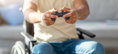 Tekerlekli sandalyedeki siyahi adamın online video oyununun keyfini sürerken, evde eğlenirken, yakın plan çekerken görüntüsü. Bilgisayar oyunu oynayan engelli Afrikalı Amerikalı adam tanınmaz halde.