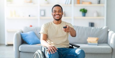 Ev eğlenceleri. Özürlü Afrikalı Amerikalı, TV kumandalı, kapalı mekanda film seyreden bir adam. Neşeli siyah adam televizyon izliyor, kanallar arasında geçiş yapıyor.