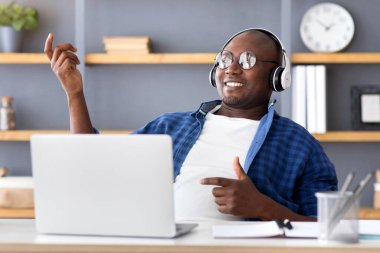 İşte mola. Neşeli siyah adam kulaklıkla müzik dinliyor ve iş yerinde sanal gitar çalıyor. Serbest çalışan dinleniyor ve uzak iş fırsatlarının tadını çıkarıyor.