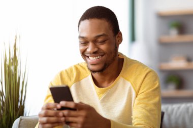 Cep telefonu kullanan ve gülümseyen Afro-Amerikalı adamın yakın çekimi. İnternetten randevu sitesi ve fotokopi alanı için yeni mobil uygulamanın tadını çıkarıyor. Modern akıllı telefonlu neşeli siyah adam, kız arkadaşıyla sohbet ediyor.
